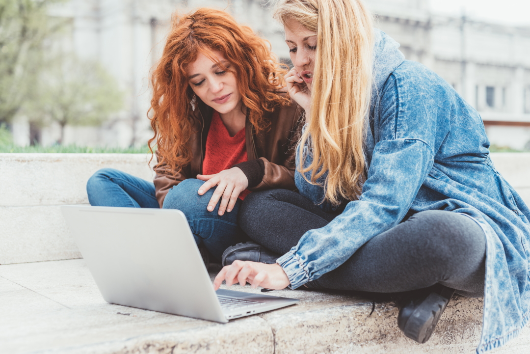 Two young women friends using computer working outdoor - business, studying, technology concept